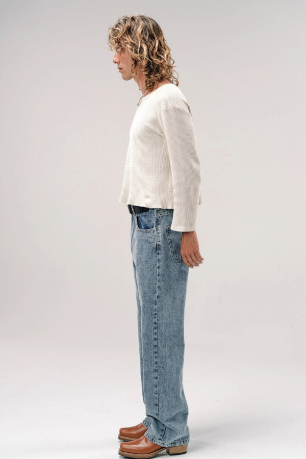 Side view of stone wash big papi denim pants on model wearing white shirt and boots, against a white background.