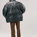 Back view of brown leather puffa jacket on model wearing brown pants and boots, against a white background.