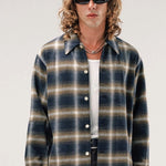 Front view of olive check logan ombre ls shirt on model wearing white shirt and grey pants, against a white background.