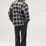 Back view of olive check logan ombre ls shirt on model wearing grey pants and boots, against a white background.