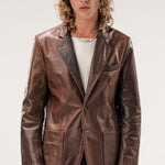 Front view of brown saico jacket on model wearing white shirt and jeans, against a white background.