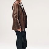 Alternate side view of brown saico jacket on model wearing white shirt, jeans and boots, against a white background.