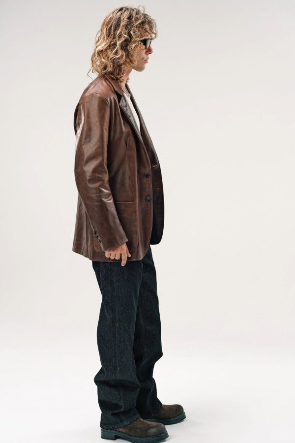 Alternate side view of brown saico jacket on model wearing white shirt, jeans and boots, against a white background.
