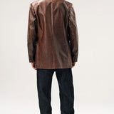 Back view of brown saico jacket on model wearing jeans and boots, against a white background.