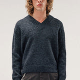 Front view of black vexed v-neck sweater on model wearing grey pants, against a white background.