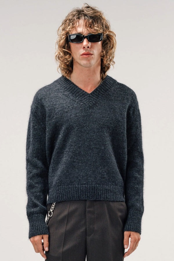 Front view of black vexed v-neck sweater on model wearing grey pants, against a white background.