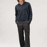 Alternate front view of black vexed v-neck sweater on model wearing grey pants and boots, against a white background.