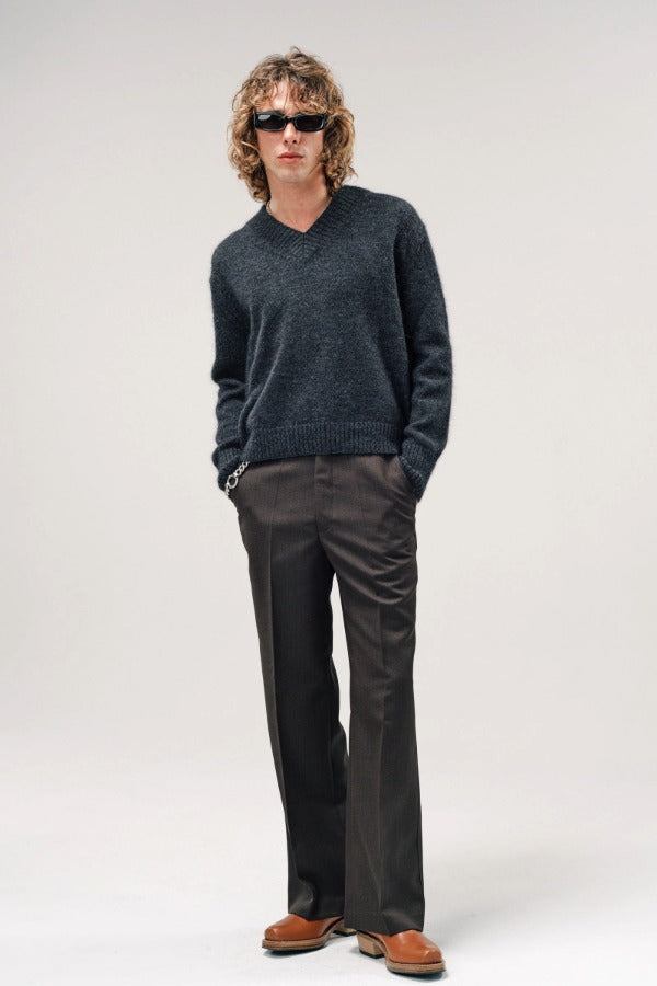 Alternate front view of black vexed v-neck sweater on model wearing grey pants and boots, against a white background.