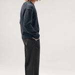 Side view of black vexed v-neck sweater on model wearing grey pants and boots, against a white background,