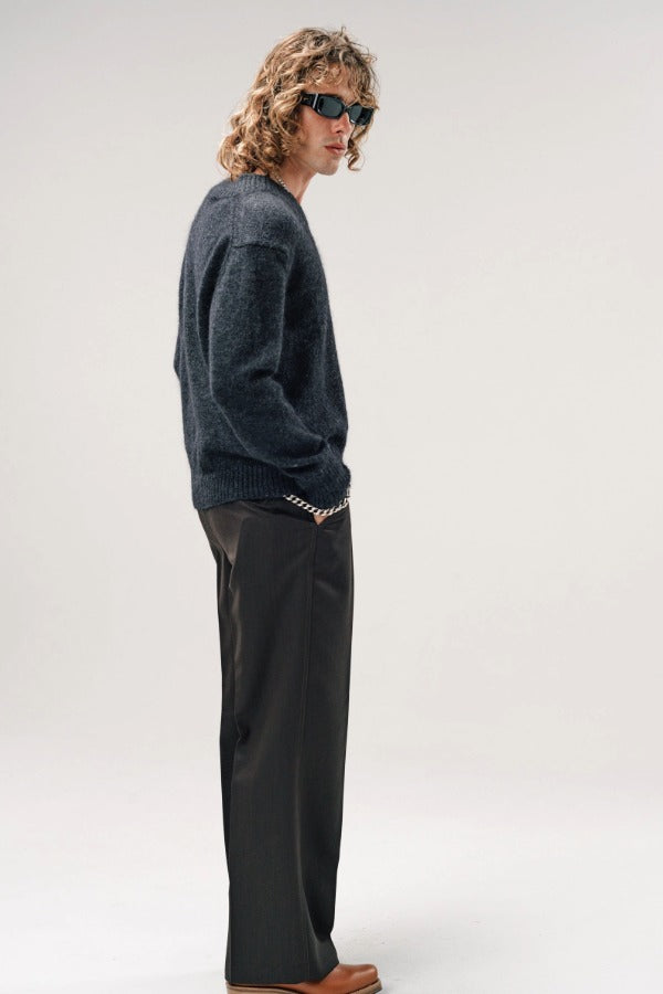 Side view of black vexed v-neck sweater on model wearing grey pants and boots, against a white background,