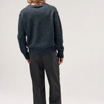 Back view of black vexed v-neck sweater on model wearing grey pants and boots, against a white background.