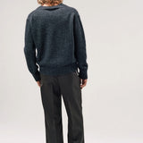 Back view of black vexed v-neck sweater on model wearing grey pants and boots, against a white background.