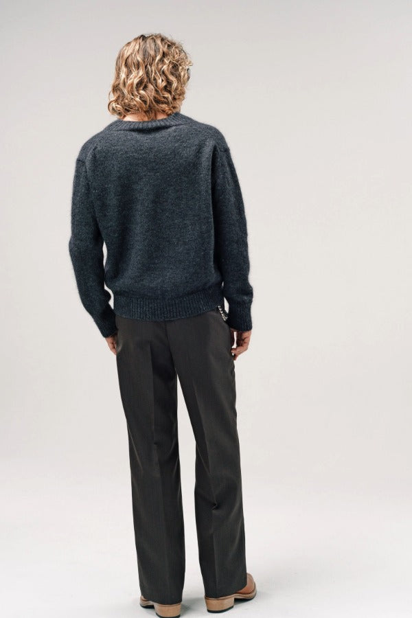 Back view of black vexed v-neck sweater on model wearing grey pants and boots, against a white background.