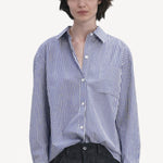 Front view of blue white stripe imny shirt on model wearing dark jeans, against a white background.