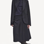 Front view of titan midnight kilt skirt on model wearing a black blazer and navy top with boots, against a white background.