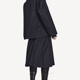 Back view of titan midnight kilt skirt on model wearing black blazer and boots, against a white background.