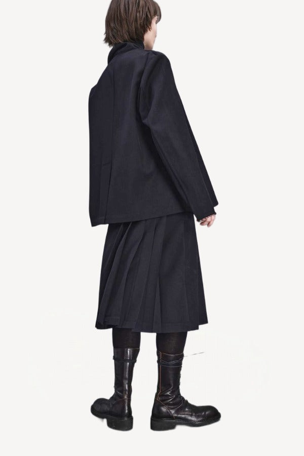Back view of titan midnight kilt skirt on model wearing black blazer and boots, against a white background.