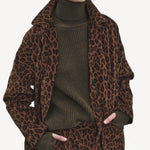 Front view of leopard work jacket on model wearing green sweater and leopard pants, against a white background.