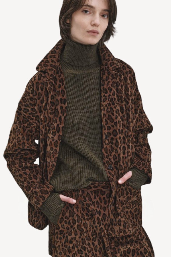 Front view of leopard work jacket on model wearing green sweater and leopard pants, against a white background.