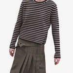 Front view of navy/oat sibs stripe sweater on model wearing plaid kilt, against a whiter background.