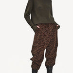 Front view of leopard yayla25 pants on model wearing green sweater and boots, against a white background.