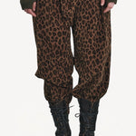 Front closeup view of leopard yayla25 pants on model wearing green sweater and boots, against a white background.