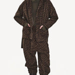 Front view of leopard yayla25 pants on model wearing green sweater, leopard jacket and boots, against a white background.