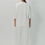 Back view of off white thebe ss cropped sweatshirt on model wearing white pants, against a white background.