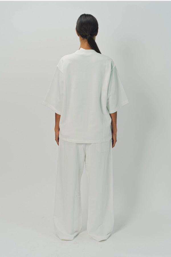 Back view of off white thebe ss cropped sweatshirt on model wearing white pants, against a white background.