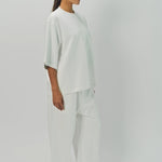 Side view of off white thebe ss cropped sweatshirt on model wearing white pants, against a white background.