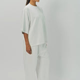 Side view of off white thebe ss cropped sweatshirt on model wearing white pants, against a white background.