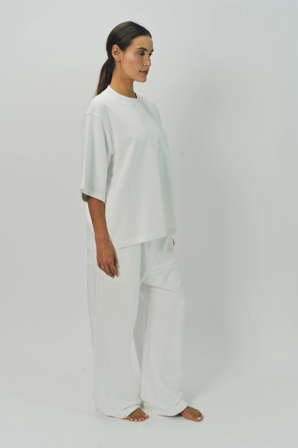 Side view of off white thebe ss cropped sweatshirt on model wearing white pants, against a white background.