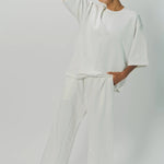 Alternate front view of off white thebe ss cropped sweatshirt on model wearing white pants, against a white background.
