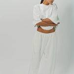 Alternate front view of off white thebe ss cropped sweatshirt on model wearing white pants, against a white background.