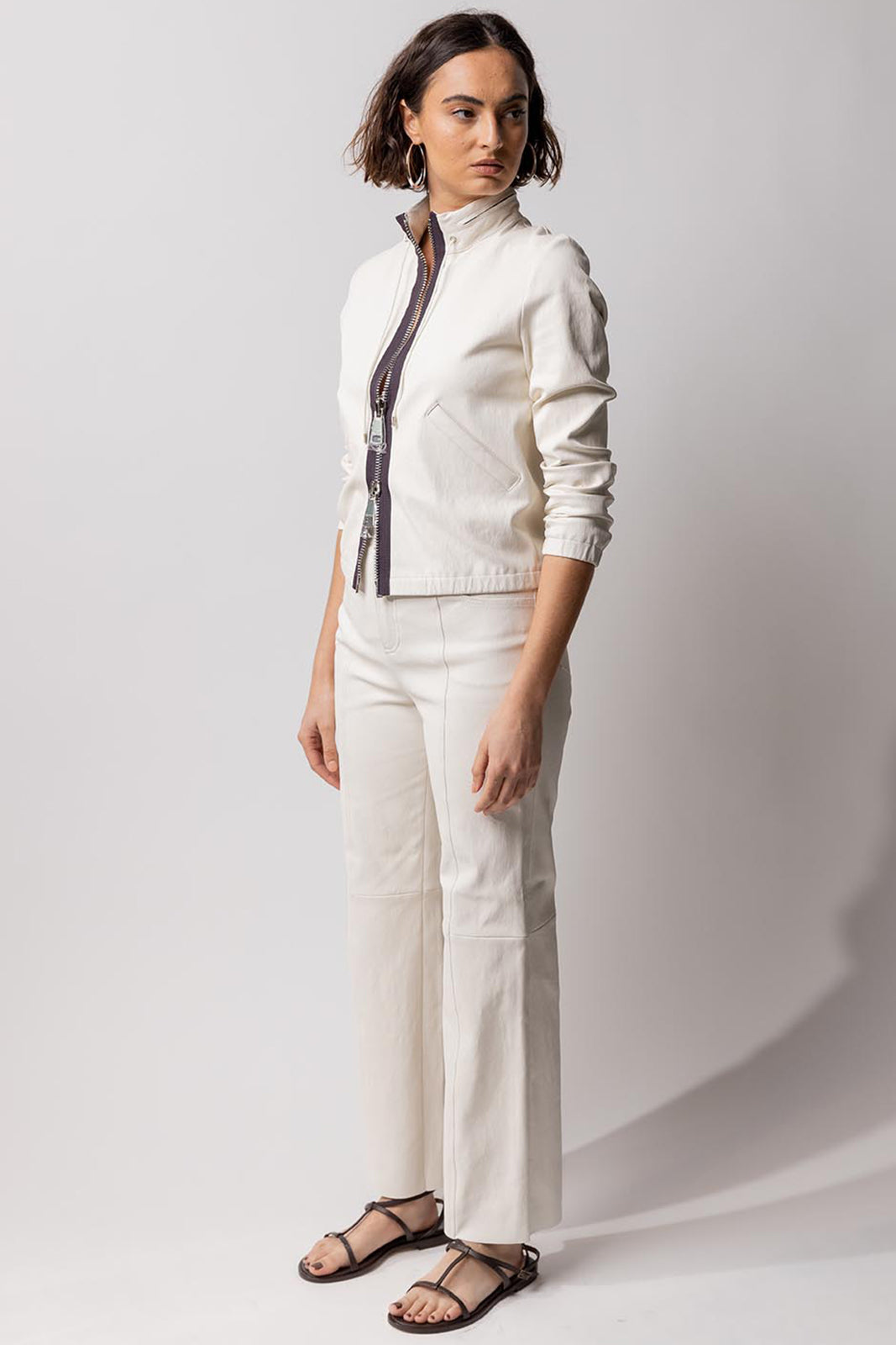 Alternate side view of white my way jacket on model wearing white leather pants, against a white background.