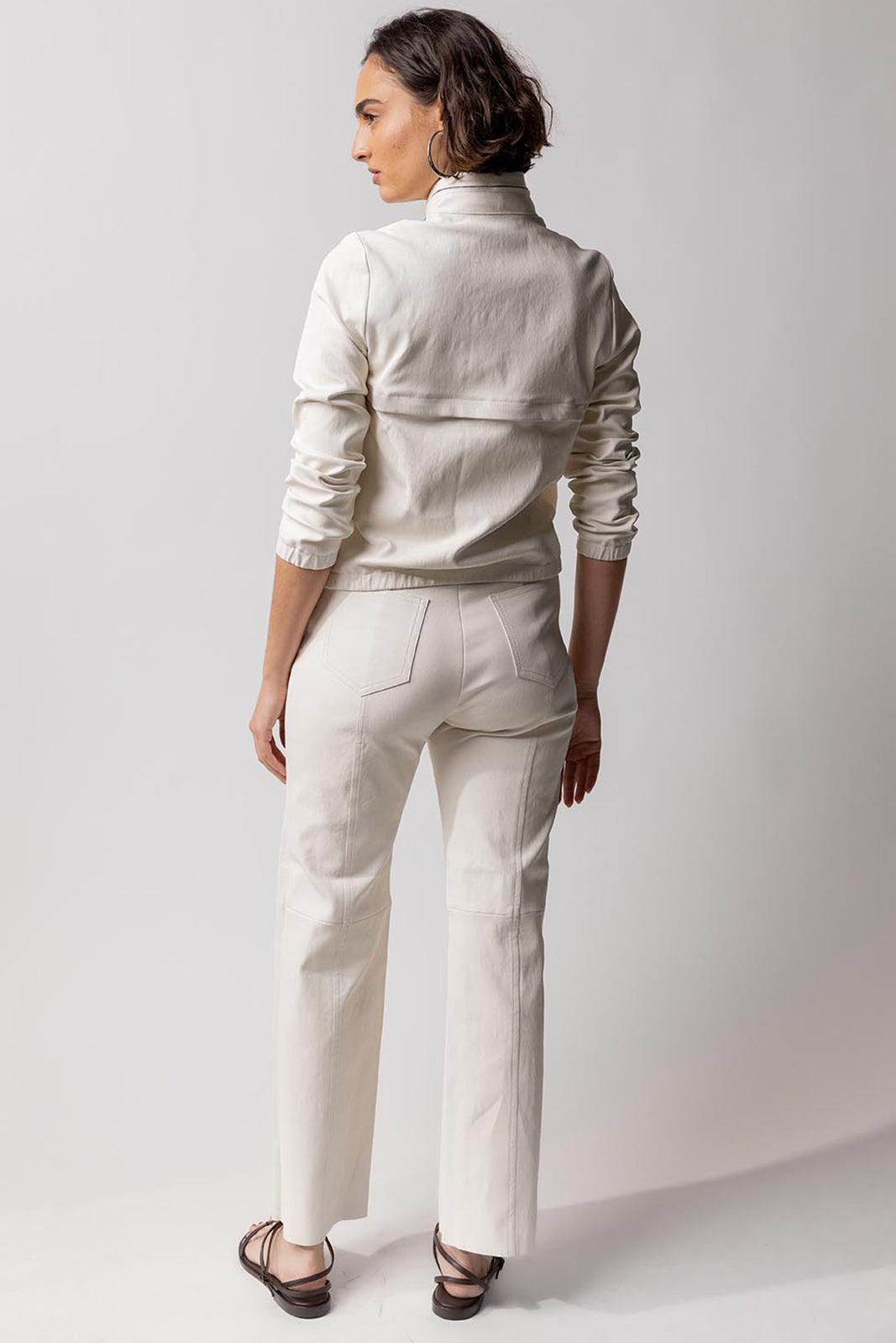 Back view of white my way jacket on model wearing white leather pants and black sandals, against a white background.