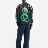 Back view of multi mythical creatures on model wearing blue trousers and black sandals, against white background.