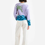 Back view of multi pal beach cardigan on model wearing white trousers and white wedge heels, against a white background.