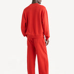 Back view of sanguinello daly crew top on dark-haired model wearing red trousers, against white background.