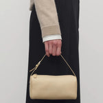 Front view of sand 90's bag on model wearing a beige sweater and black pants, against a white background.