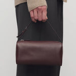 Front view of burgundy 90's bag on model wearing grey pants and ecru sweater, against a white background.