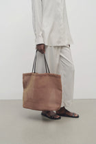 Front view of mesh and leather bag in acero on white background, with model  wearing light silk suit and sandals.