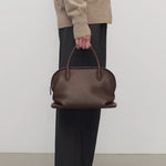 Front view of deep brown agnes bag on model wearing grey pants and ecru sweater, against a white background.