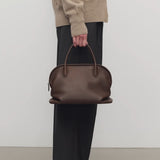Front view of deep brown agnes bag on model wearing grey pants and ecru sweater, against a white background.