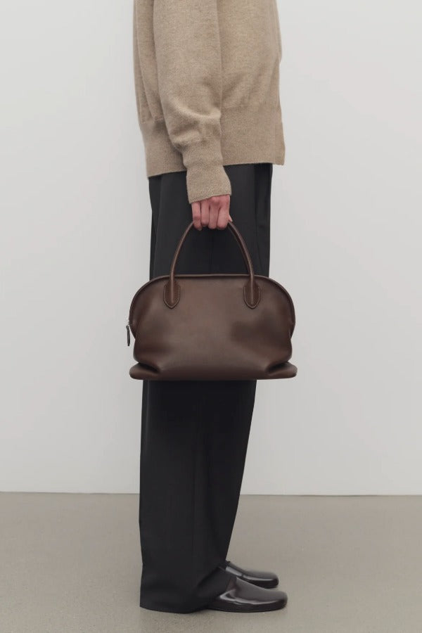 Front view of deep brown agnes bag on model wearing grey pants and ecru sweater, against a white background.