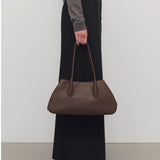 Front view of deep brown alger shoulder bag on model wearing black pants and brown melange sweater, against a white background.