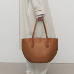 Front view of cuir alger tote on model wearing snow trench coat and loafers, against a white background.