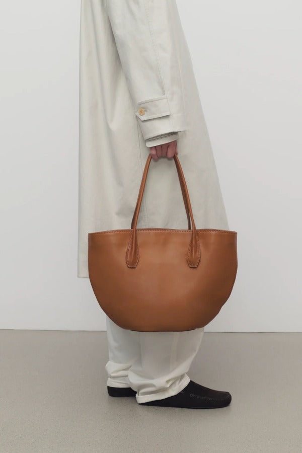 Front view of cuir alger tote on model wearing snow trench coat and loafers, against a white background.