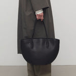 Front view of black alger tote on model wearing khaki pants, dark green coat, and loafers against a white background.