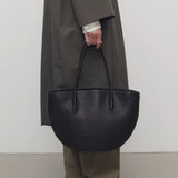 Front view of black alger tote on model wearing khaki pants, dark green coat, and loafers against a white background.